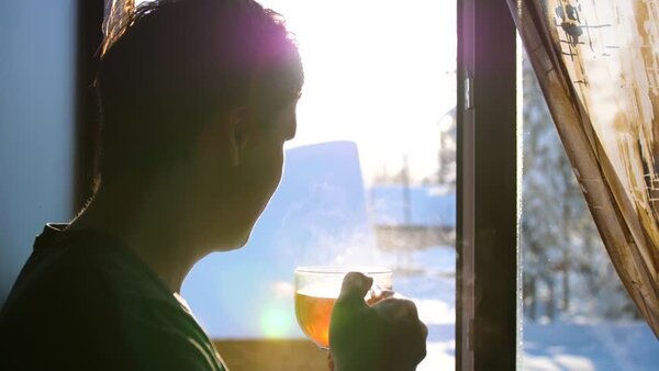 Adult ținând o cană de ceai, privirea îndreptată spre fereastră după plimbare